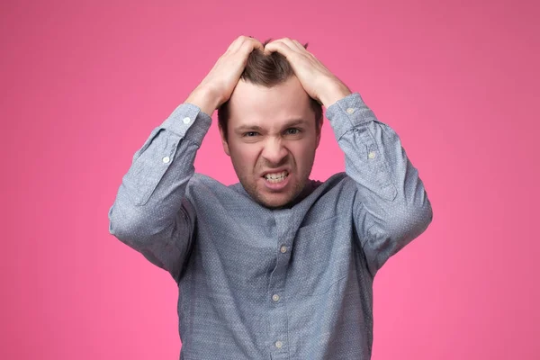 Enojado joven gritando poniendo las manos en la cabeza en la pared rosa en el estudio . —  Fotos de Stock