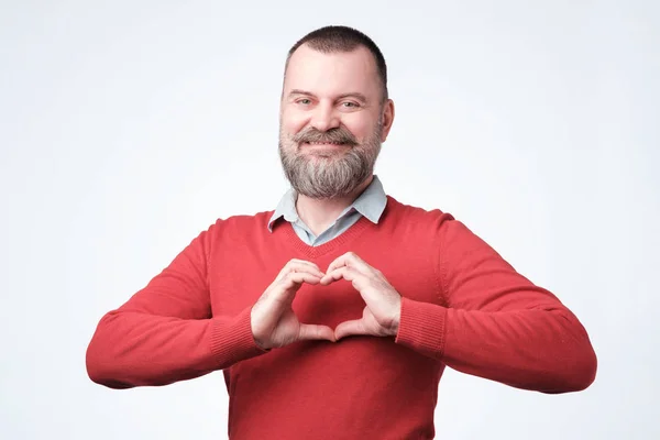 Volwassen Europese man met baard maken uit de handen hart. — Stockfoto