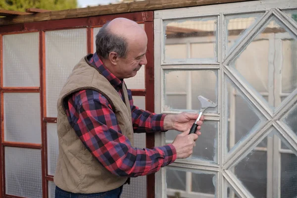 Senior pelato uomo contadino pulisce la finestra dalla vernice . — Foto Stock