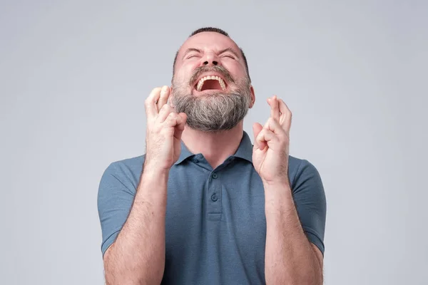 Volwassen bebaarde man Crossing vingers en gesloten ogen, vragen om geluk. — Stockfoto