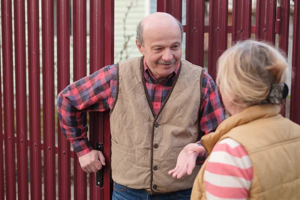 Two senior neighbors takling to each other on sunny day near fence. — Stock Photo, Image