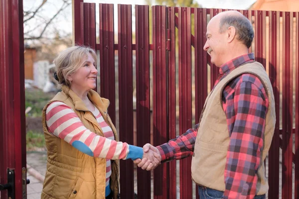 Two senior neighbors takling to each other on sunny day near fence. — Stock Photo, Image