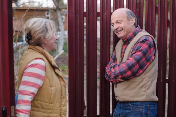 Två Senior grannar takling till varandra på soliga dag nära staket. — Stockfoto