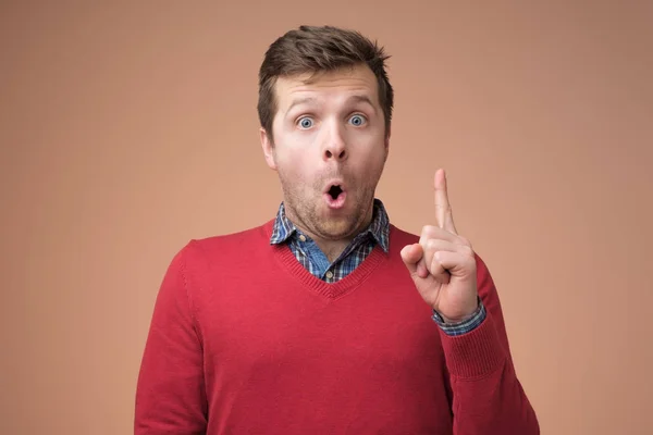 Attractive young man in red sweater pointing up with his finger — Stock Photo, Image