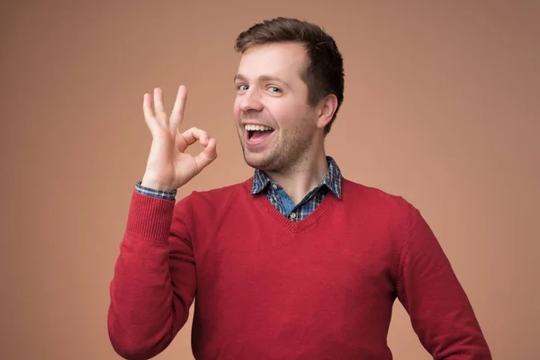 Young man in red sweater gesturing ok sign — Stock Photo, Image