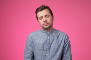 Pembe arka planda gözleri kapalı duran beyaz bir genç..