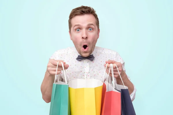 man holding pile of bags with gifts with shock