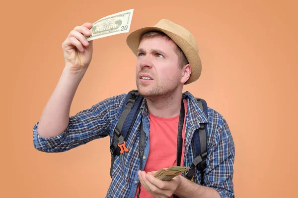 Турист у капелюсі тримає долар банкноту, перевіряючи його — стокове фото