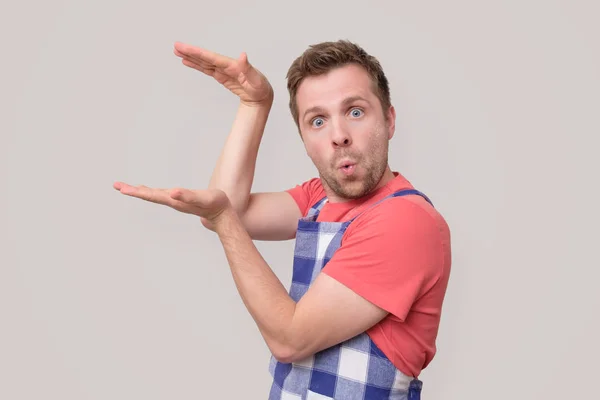 Young man in apron show big size by fingers demonstrate measure — Stock Photo, Image