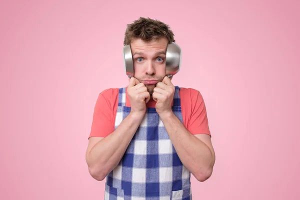 Hombre en delantal cubriéndose las orejas con sartenes . — Foto de Stock