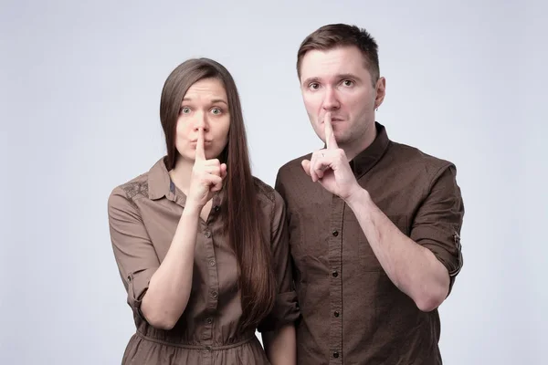 Young man and woman holding their fingers on lips asking to be silent — Stock Photo, Image