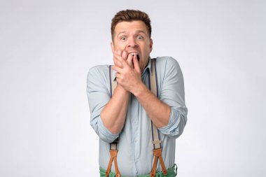 Gömlekli genç bir adam ve pantolon askısı. Ağzı, elleri ve şokla kapatıyor.