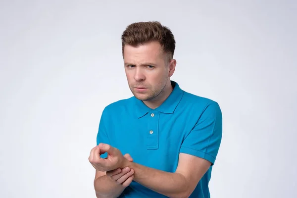 Hombre joven en camiseta azul mantiene la mano en la muñeca, comprueba el pulso o la frecuencia cardíaca, cuida de su salud —  Fotos de Stock