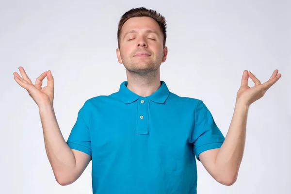 Joven hombre guapo en camiseta azul relajante y sonriente con los ojos cerrados haciendo gesto de meditación —  Fotos de Stock