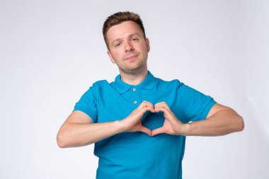 Mavi gömlekli yakışıklı adam elleriyle kalp yapıyor