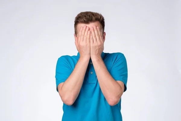Молодий білий чоловік у блакитній сорочці закриває обличчя руками, намагаючись залишитися анонімним . — стокове фото