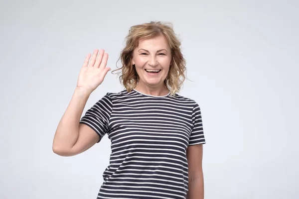 Positieve volwassen Kaukasische vrouw vriendelijk glimlachend en zwaaiend hand op camera — Stockfoto