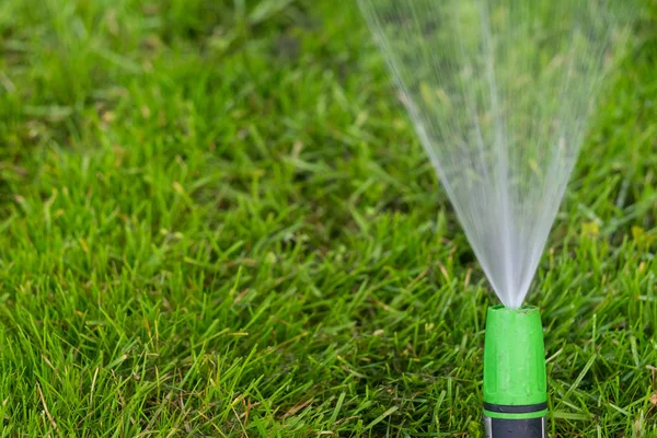 Nawadnianie zielonego trawnika z opryskiwaczem w letni dzień — Zdjęcie stockowe