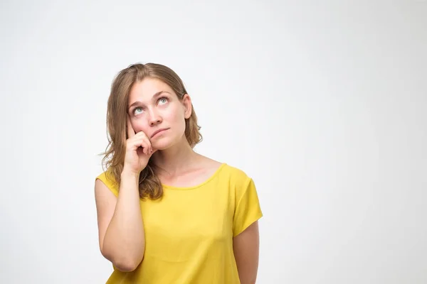 Young woman looks with doubt wears yellow t shirt, trying to make right decision — Stock Photo, Image