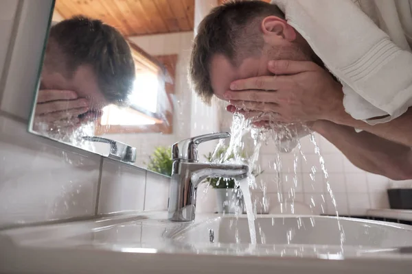 Uomo caucasico che lava la faccia in un lavandino in un bagno bianco — Foto Stock