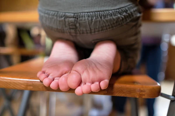 Child is sitting on chair in room. Legs and feet of kids