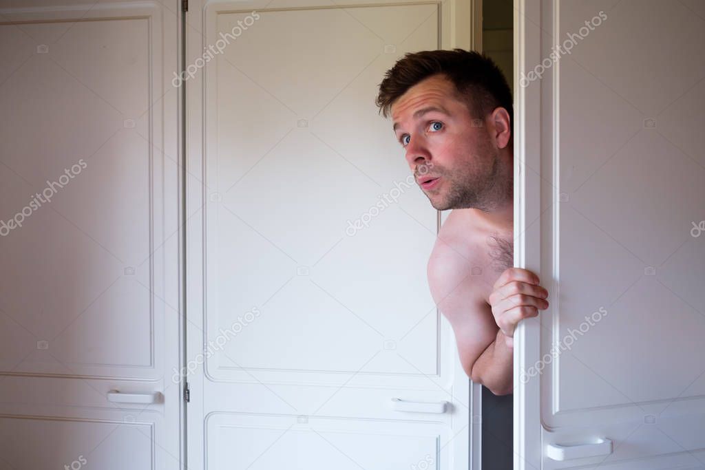 Young caucasian naked man hiding in wardrobe