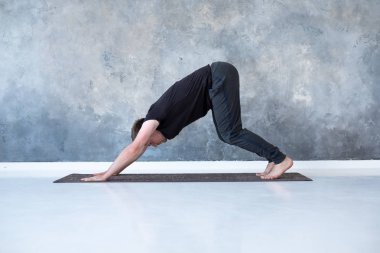 Egzersiz yapan genç bir adam, yoga yapıyor, köpek pozisyonuna bakıyor.