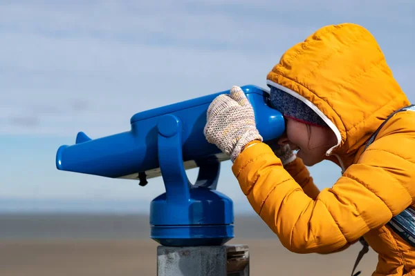 Mujer con abrigo amarillo mirando al mar usando binocular operado con monedas — Foto de Stock