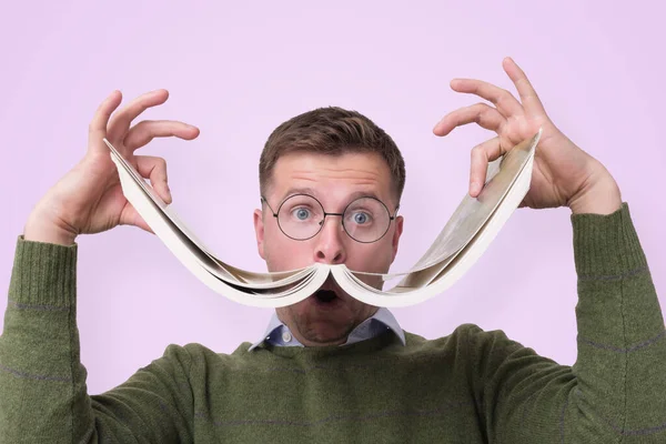 Estudante masculino caucasiano engraçado em óculos segurando livro como um bigode . — Fotografia de Stock