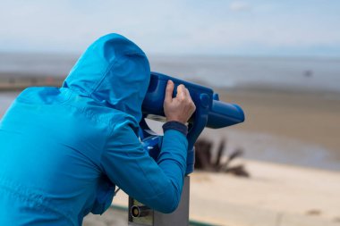 Mavi ceketli adam denizlere bakıyor. Parayla çalışan dürbün görüntüler kullanıyor.