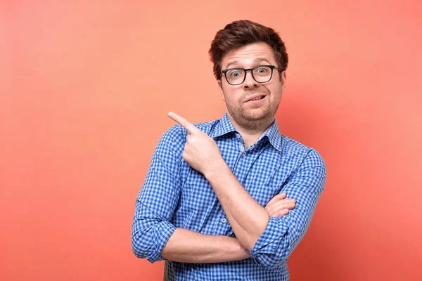 Confuso homem perplexo em óculos e camisa azul apontando dedo de lado — Fotografia de Stock