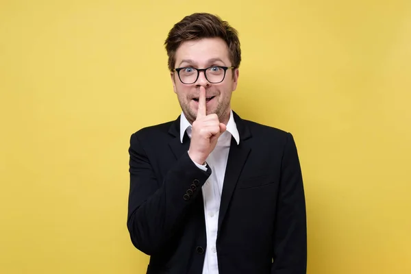 Hombre de traje sobre fondo amarillo mostrando un gesto de silencio — Foto de Stock