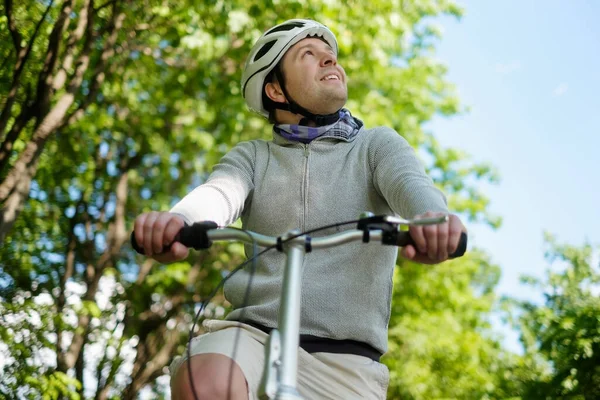 Man i hjälm cykling utomhus i skogen ler en solig dag — Stockfoto