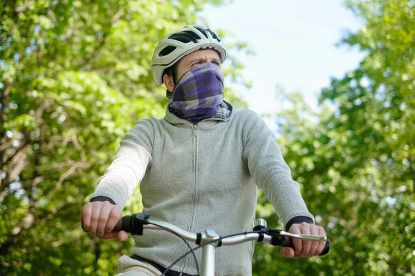 Ung kauakasisk man i hjälm cykling utomhus i skogen stänga ansiktet med halsduk — Stockfoto