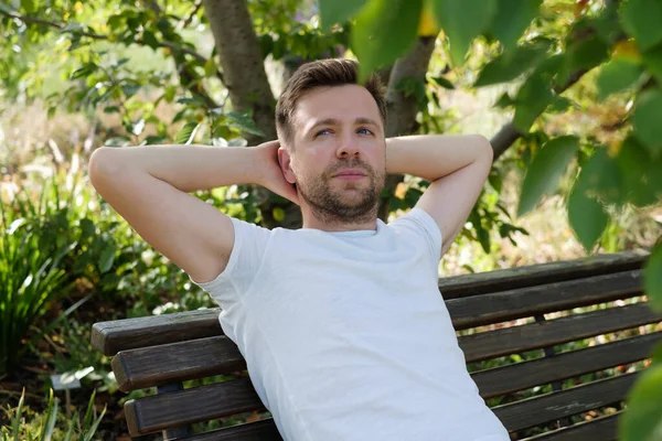 Een jongeman zittend op een bankje in het park en rustend. — Stockfoto