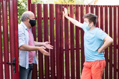 Two men in medical mask speaking to each other, discuss problems on sunny day clipart