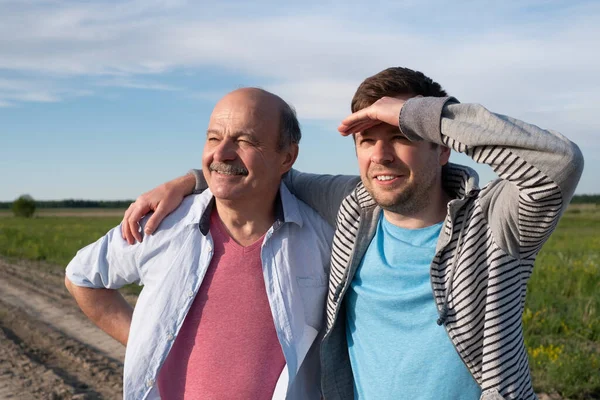 Mature caucasian father and his son looking aside camera standing in the field. — Stock Photo, Image
