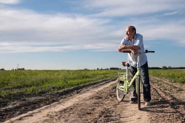 Gammel mand ridning en cykel på banen hviler på den solrige dag - Stock-foto