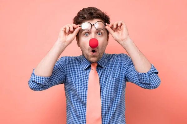 Uomo con naso rosso pagliaccio guardando attraverso gli occhiali in sorpresa. — Foto Stock