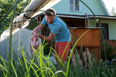 Bahçesinde çiçeklerini sulayan genç bir adam.