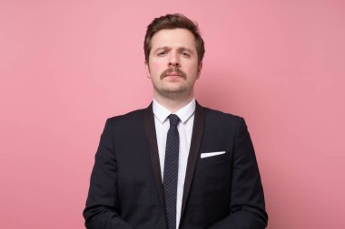 Takım elbiseli yakışıklı genç adam kameraya ciddi ve kendinden emin bakıyor..