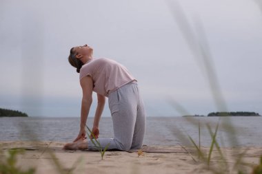 Beyaz kadın deve yapıyor. Ustrasana asana 'ya dışarıda egzersiz yaptırıyor..