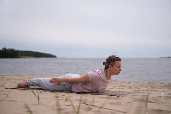 Кавказка практикует йогу, делает салабхасану позу вариации на пляже — стоковое фото