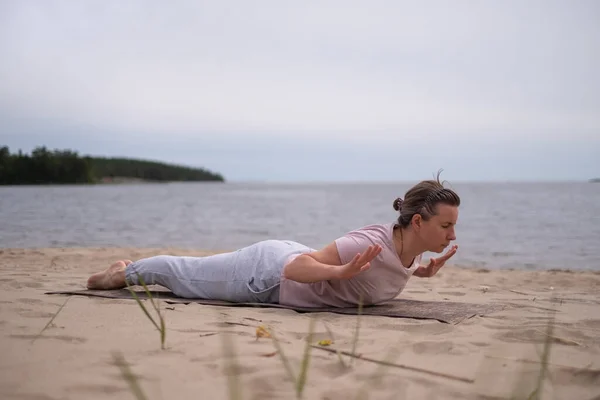 Кавказка практикует йогу, делает салабхасану позу вариации на пляже — стоковое фото