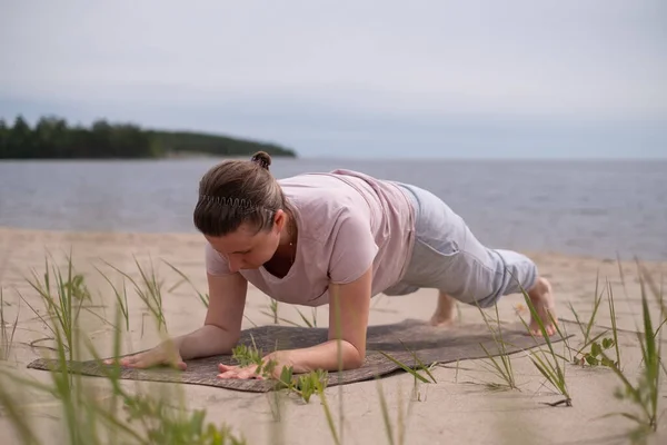 Mladá žena dělá prkno pozice venku na pláži. — Stock fotografie