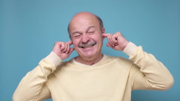 Homme âgé essayant de boucher les oreilles sur fond bleu. — Video