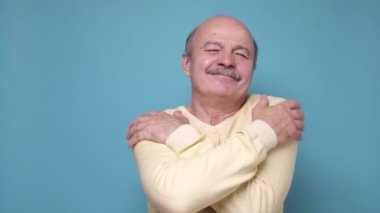 Kıdemli yakışıklı adam kendine mutlu ve pozitif sarılıyor, sırıtıyor.