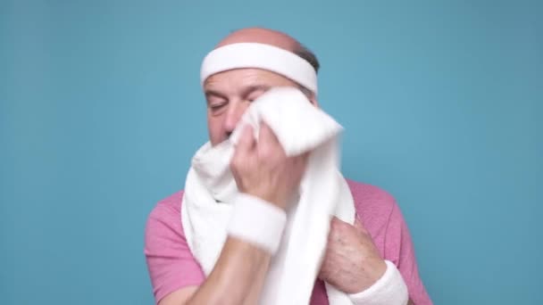 Viejo cansado con bigote limpiando el sudor después del entrenamiento deportivo en la pared azul. — Vídeos de Stock