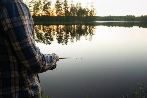 Bir adam oltayla balık tutuyor, gölün kıyısında duruyor.