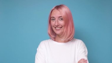 Çekici gülüşü ve boyalı pembe saçı olan kadın kameraya bakıyor.